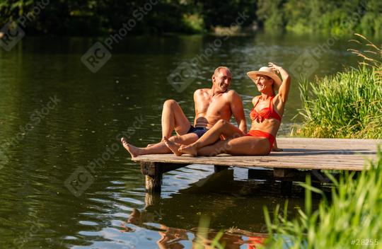 Mature couple joyfully relaxing on a wooden dock, woman adjusting hat and man smiling at her, in a serene lake setting at summer in germany  : Stock Photo or Stock Video Download rcfotostock photos, images and assets rcfotostock | RC Photo Stock.: