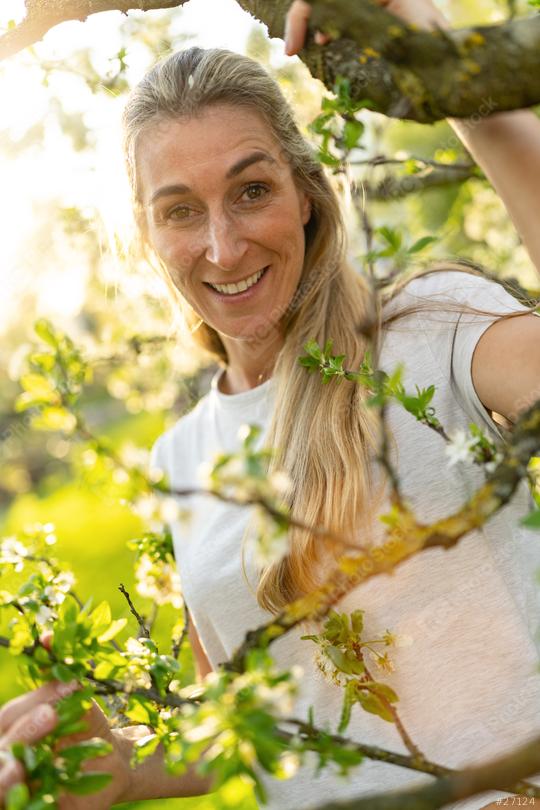 Mature woman smiling in a sunlit garden, peeking through flowering tree branches  : Stock Photo or Stock Video Download rcfotostock photos, images and assets rcfotostock | RC Photo Stock.: