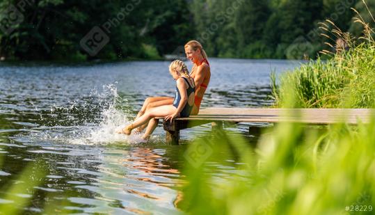 Mother and daughter laughing and splashing water while sitting on a dock at a river surrounded by greenery at summer in germany  : Stock Photo or Stock Video Download rcfotostock photos, images and assets rcfotostock | RC Photo Stock.: