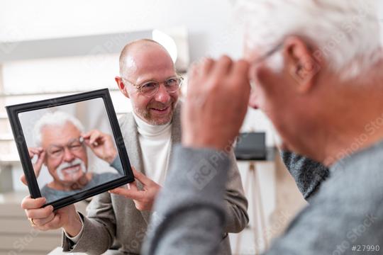 Optician holding a mirror for a older customer trying on glasses in a optician store  : Stock Photo or Stock Video Download rcfotostock photos, images and assets rcfotostock | RC Photo Stock.: