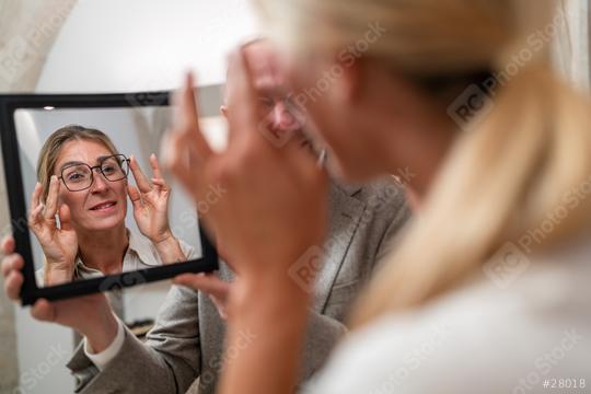 Optician holding a mirror to female customer trying on glasses in a optical store.  : Stock Photo or Stock Video Download rcfotostock photos, images and assets rcfotostock | RC Photo Stock.: