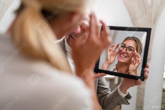 Optician holding a mirror to smiling woman trying on glasses in a optical store.  : Stock Photo or Stock Video Download rcfotostock photos, images and assets rcfotostock | RC Photo Stock.: