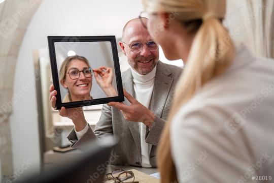 Optician holding a mirror to smiling woman trying on new glasses in a optical store.  : Stock Photo or Stock Video Download rcfotostock photos, images and assets rcfotostock | RC Photo Stock.: