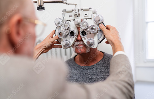 Optometrist adjusting phoropter for senior patient