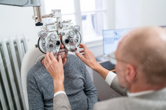 Optometrist adjusting phoropter for senior patient