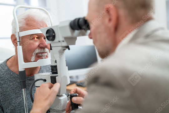 Optometrist using a slit lamp to examine a senior man