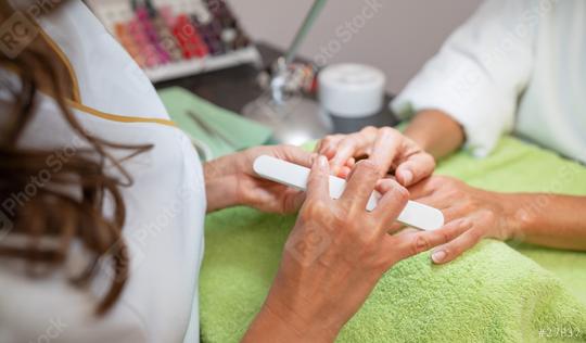 Over-the-shoulder view of a manicurist filing a client