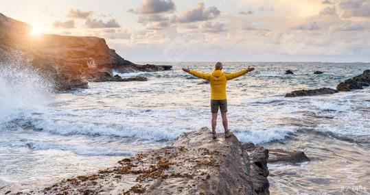 Person in yellow jacket standing on rock by the sea with arms wide open at sunset  : Stock Photo or Stock Video Download rcfotostock photos, images and assets rcfotostock | RC Photo Stock.: