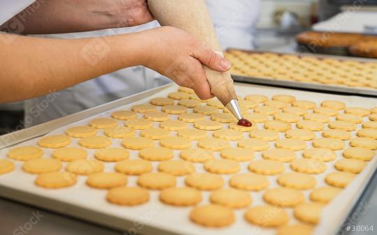 Piping red jam onto freshly baked cookies arranged on a baking sheet. Rows of plain cookies are being prepared for assembly, creating a jam-filled sandwich cookie.  : Stock Photo or Stock Video Download rcfotostock photos, images and assets rcfotostock | RC Photo Stock.: