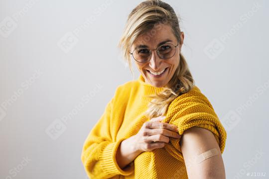 Portrait of a mature woman with glasses smiling after getting a corona vaccine. Woman holding up her shirt sleeve and showing her arm with bandage after receiving vaccination.  : Stock Photo or Stock Video Download rcfotostock photos, images and assets rcfotostock | RC Photo Stock.: