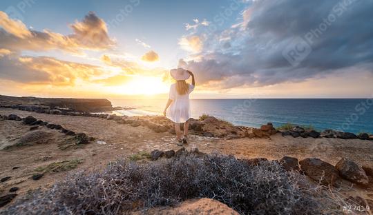 Rear view of a woman in white holding hat looking at the sea during sunset on rocky coast at Playa de Cofete, Fuerteventura, Canary Islands.  : Stock Photo or Stock Video Download rcfotostock photos, images and assets rcfotostock | RC Photo Stock.: