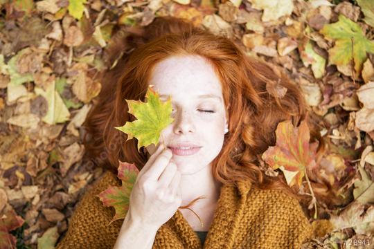 Red-haired woman lying on autumn leaves, holding a maple leaf over one eye, with her eyes closed, embracing the serene and colorful essence of fall in a cozy and peaceful outdoor setting  : Stock Photo or Stock Video Download rcfotostock photos, images and assets rcfotostock | RC Photo Stock.:
