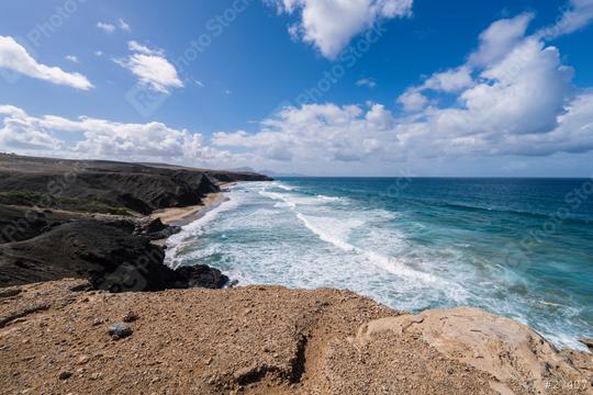 Scenic Fuerteventura beach view of waves hitting the rocky coastline under a blue sky with fluffy clouds  : Stock Photo or Stock Video Download rcfotostock photos, images and assets rcfotostock | RC Photo Stock.: