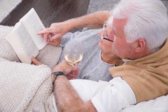 Senior couple enjoying a cozy moment together on a couch, reading a book while holding a glass of white wine, wrapped in soft blankets, symbolizing relaxation, love, and companionship in a warm settin  : Stock Photo or Stock Video Download rcfotostock photos, images and assets rcfotostock | RC Photo Stock.: