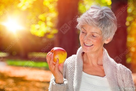 Smiling elderly woman holding an apple outdoors in autumn sunlight with a serene background  : Stock Photo or Stock Video Download rcfotostock photos, images and assets rcfotostock | RC Photo Stock.: