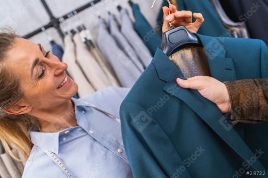 Smiling sailswoman showing a teal jacket to a male customer, clothes racks in the background at weeding store  : Stock Photo or Stock Video Download rcfotostock photos, images and assets rcfotostock | RC Photo Stock.: