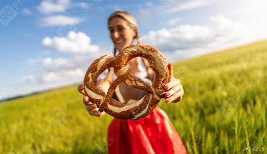 Smiling woman in Bavarian dirndl holding a large pretzel in front of a wheat field celebrating Oktoberfest or dult festival in munich.  : Stock Photo or Stock Video Download rcfotostock photos, images and assets rcfotostock | RC Photo Stock.: