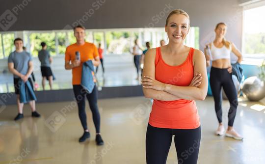 Smiling woman in orange tank top with arms crossed in a gym, people in the background. Teamwork Concept image  : Stock Photo or Stock Video Download rcfotostock photos, images and assets rcfotostock | RC Photo Stock.: