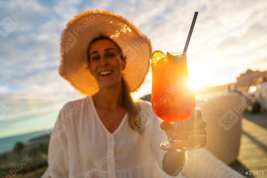 Smiling woman in straw hat holding a cocktail against a sunset backdrop  : Stock Photo or Stock Video Download rcfotostock photos, images and assets rcfotostock | RC Photo Stock.: