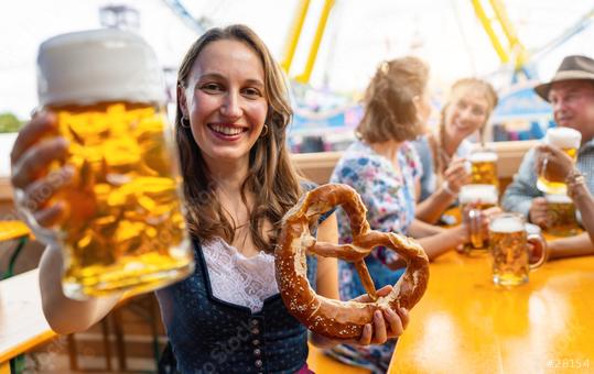 Smiling woman in traditional dress or dirndl holding a beer mug and a pretzel, with friends drinking in the background at oktoberfest in munich or dult in germany  : Stock Photo or Stock Video Download rcfotostock photos, images and assets rcfotostock | RC Photo Stock.: