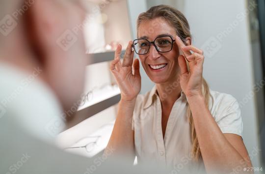 Smiling woman trying on black framed glasses. Optician in foreground and eyewear shop interior in the background.  : Stock Photo or Stock Video Download rcfotostock photos, images and assets rcfotostock | RC Photo Stock.: