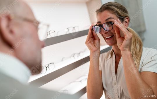 Smiling woman trying on black framed glasses. Optician in foreground. Eyewear shop interior  : Stock Photo or Stock Video Download rcfotostock photos, images and assets rcfotostock | RC Photo Stock.: