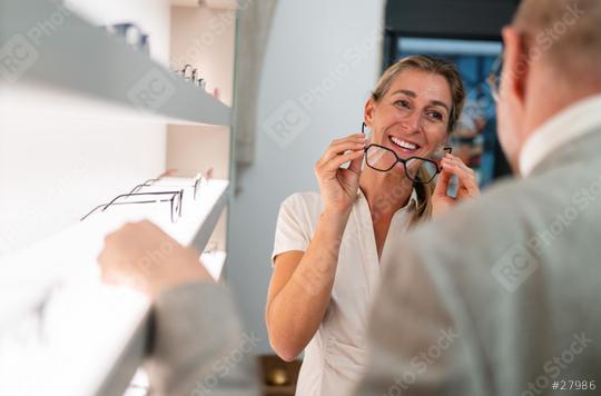 Smiling woman trying on black framed glasses. optician in foreground and eyewear shop interior in the background.  : Stock Photo or Stock Video Download rcfotostock photos, images and assets rcfotostock | RC Photo Stock.: