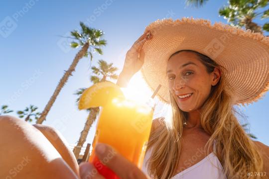 smiling woman wearing a straw hat and holding a tropical cocktail with palm trees in the background at a hotel  : Stock Photo or Stock Video Download rcfotostock photos, images and assets rcfotostock | RC Photo Stock.: