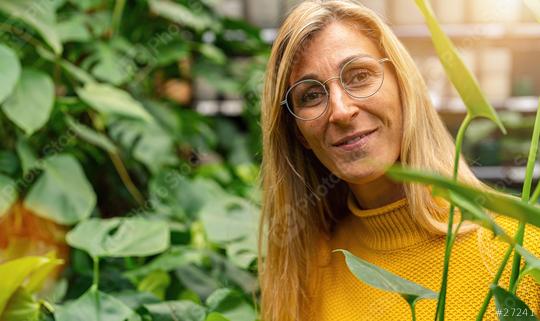 Smiling woman with glasses amidst green flowers looking in to camera in a Garden Center for Purchase. Shopping in a greenhouse concept image  : Stock Photo or Stock Video Download rcfotostock photos, images and assets rcfotostock | RC Photo Stock.: