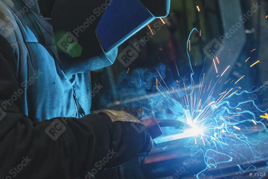 strong man is a welder, in a welding mask and welders leathers, a metal product is welded with a welding machine in the garage, blue sparks fly to the sides   : Stock Photo or Stock Video Download rcfotostock photos, images and assets rcfotostock | RC Photo Stock.: