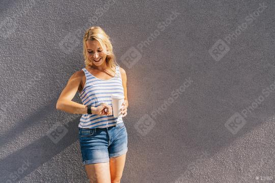 Stylish happy young woman looking to her clock. She holds paper coffee to go and enjoying the sunlight in the city. portrait of smiling girl , lifestyle concept image.  : Stock Photo or Stock Video Download rcfotostock photos, images and assets rcfotostock | RC Photo Stock.: