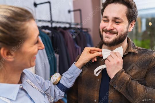 Tailor adjusting a bow tie for a smiling male customer, clothes racks in a wedding shop  : Stock Photo or Stock Video Download rcfotostock photos, images and assets rcfotostock | RC Photo Stock.: