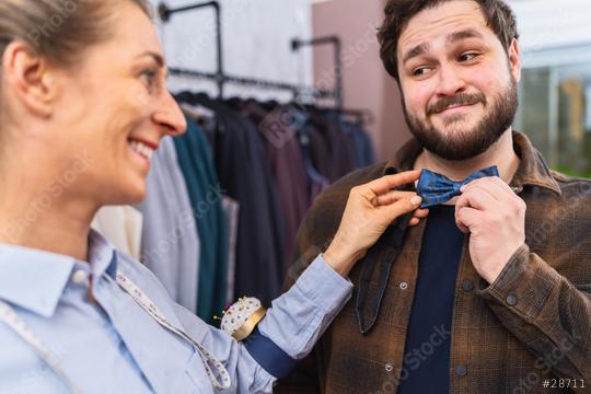 Tailor fitting a blue bow tie on a customer, both smiling, with clothing in background  : Stock Photo or Stock Video Download rcfotostock photos, images and assets rcfotostock | RC Photo Stock.: