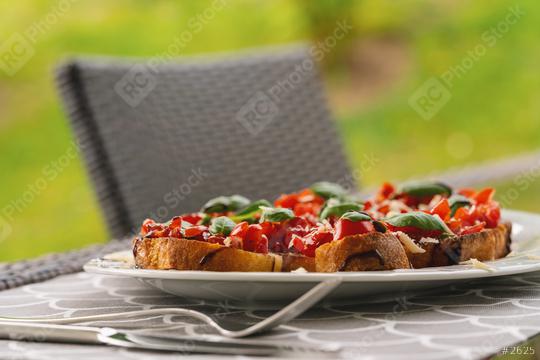 Tasty savory tomato Italian appetizers, or bruschetta, on slices of toasted baguette garnished with basil, close up on a Plate on a table outside  : Stock Photo or Stock Video Download rcfotostock photos, images and assets rcfotostock | RC Photo Stock.: