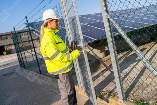 Technician in high visibility jacket on a gate with walkie-talkie at solar farm. Alternative energy ecological concept image.  : Stock Photo or Stock Video Download rcfotostock photos, images and assets rcfotostock | RC Photo Stock.: