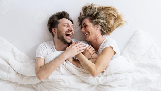 Top view of young loving couple lying on bed laughing and smiling with blanket. They are looking at each other with trust in love  : Stock Photo or Stock Video Download rcfotostock photos, images and assets rcfotostock | RC Photo Stock.: