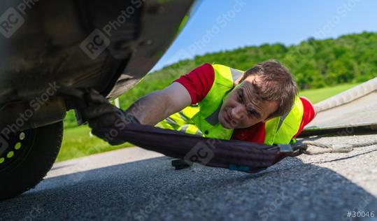 Tow truck worker inspecting a car underneath after an accident to prepare it with tow rope for transport on the roadside  : Stock Photo or Stock Video Download rcfotostock photos, images and assets rcfotostock | RC Photo Stock.: