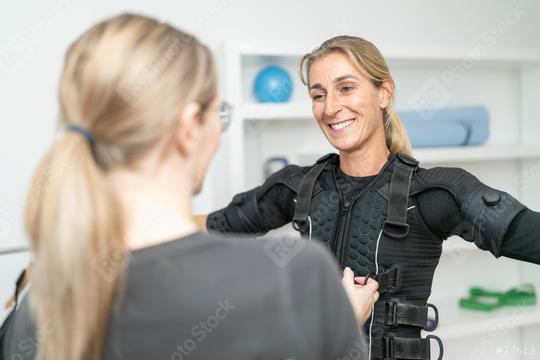 Trainer assisting a smiling woman by wearing an EMS training suit bevor training exercise in a EMS - Studio  : Stock Photo or Stock Video Download rcfotostock photos, images and assets rcfotostock | RC Photo Stock.: