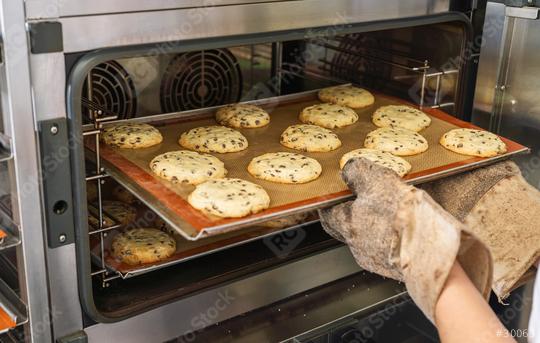 tray of freshly baked chocolate chip cookies is being taken out of the oven using protective oven mitts. The cookies are golden and placed on a silicone baking mat.  : Stock Photo or Stock Video Download rcfotostock photos, images and assets rcfotostock | RC Photo Stock.: