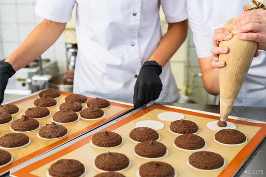 Two bakers are piping gingerbread dough onto wafers, preparing the cookies for baking. One baker is using a piping bag while the other is arranging wafers on a baking sheet  : Stock Photo or Stock Video Download rcfotostock photos, images and assets rcfotostock | RC Photo Stock.: