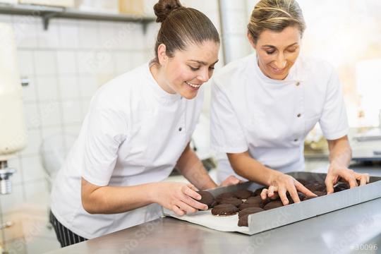 Two bakers arranging chocolate-covered gingerbreads on a tray in a bakery, carefully preparing the freshly made treats in a professional baking environment  : Stock Photo or Stock Video Download rcfotostock photos, images and assets rcfotostock | RC Photo Stock.: