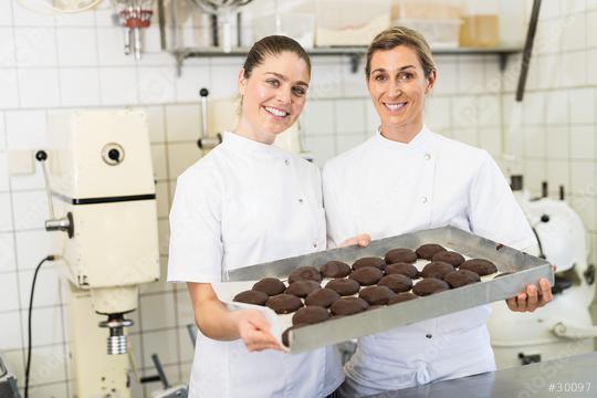Two bakers smiling and holding a tray of chocolate-covered gingerbreads in a bakery, proudly presenting their freshly made treats in a professional baking environment  : Stock Photo or Stock Video Download rcfotostock photos, images and assets rcfotostock | RC Photo Stock.:
