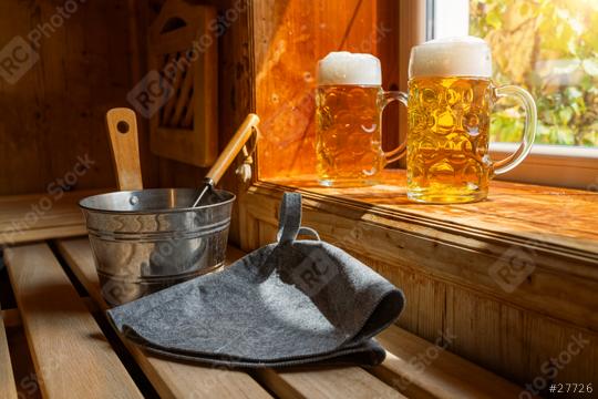 Two beer mugs with frothy beer rest on a ledge, catching sunlight. Nearby, a metal bucket, a ladle, and finnish Sauna hats on a wooden bench.  spa and wellness concept image  : Stock Photo or Stock Video Download rcfotostock photos, images and assets rcfotostock | RC Photo Stock.: