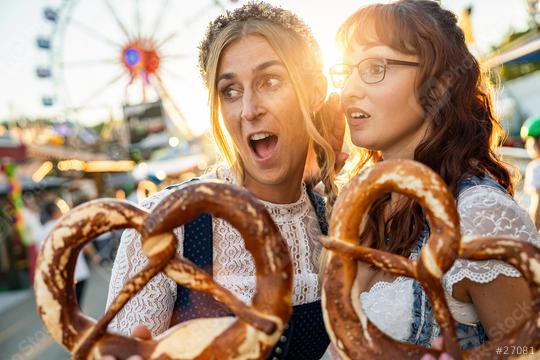 Two girlfriends look amazed with pretzel or brezen on a Bavarian fair or oktoberfest or duld in national costume or Dirndl  : Stock Photo or Stock Video Download rcfotostock photos, images and assets rcfotostock | RC Photo Stock.: