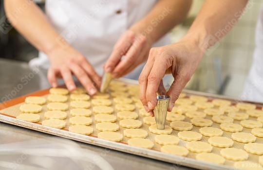 Two people are preparing cookies by cutting out the center of dough shapes on a baking tray using metal cutters. The dough is arranged neatly on a silicone baking mat.  : Stock Photo or Stock Video Download rcfotostock photos, images and assets rcfotostock | RC Photo Stock.: