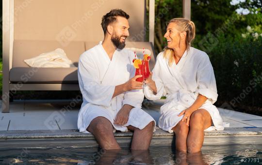 Two people in white bathrobes laughing and toasting with red drinks by a pool at sunset at a spa hotel  : Stock Photo or Stock Video Download rcfotostock photos, images and assets rcfotostock | RC Photo Stock.: