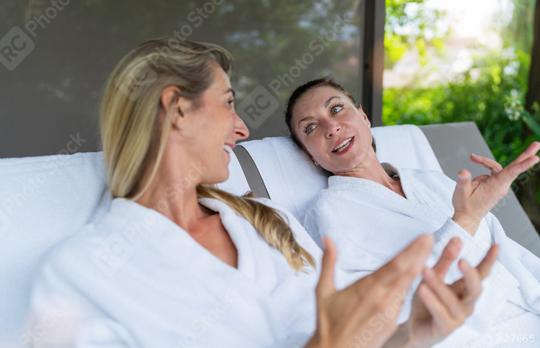 Two women in white bathrobes talking and gesturing on outdoor loungers at a spa wellness resort  : Stock Photo or Stock Video Download rcfotostock photos, images and assets rcfotostock | RC Photo Stock.: