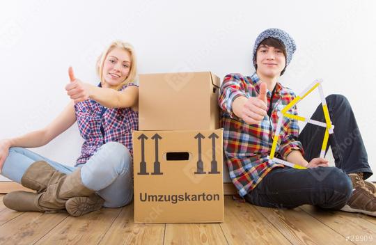 Two young people sitting on a wooden floor with moving boxes, smiling and giving thumbs up, with a measuring tool shaped like a house symbolizing a new home  : Stock Photo or Stock Video Download rcfotostock photos, images and assets rcfotostock | RC Photo Stock.: