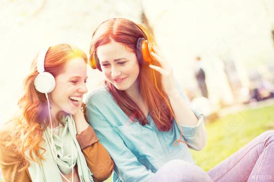 Two young red-haired women wearing headphones share a fun and cheerful moment outdoors, enjoying music together in a bright and sunny park setting.  : Stock Photo or Stock Video Download rcfotostock photos, images and assets rcfotostock | RC Photo Stock.: