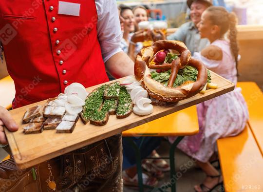 Waiter in red vest serving traditional German food on a wooden platter to a group of people in a beer tent at a oktoberfest festival or dult in germany  : Stock Photo or Stock Video Download rcfotostock photos, images and assets rcfotostock | RC Photo Stock.: